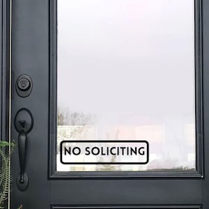 May include: A black door with a glass window. A white and black rectangular sign that reads "NO SOLICITING" is affixed to the glass. The door has a black handle and a lock.