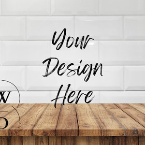 May include: A mock-up image featuring a wooden table in the foreground with the text "Your Design Here" in black script. The background is a white tiled wall. A logo with the letters "W" and "D" is in the lower left corner.