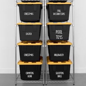May include: A metal shelving unit holds eight black storage bins with yellow lids. Each bin is labeled with white text: Christmas, Fall Decorations, Easter, Pool Toys, Christmas, Halloween, Camping Gear, and Sleeping Bags. The bins are organized on a wire rack.
