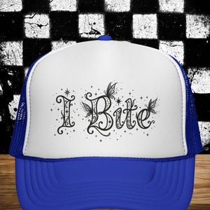 Peut inclure: Une casquette trucker blanche et bleue avec une impression graphique noire sur le panneau avant. Le motif affiche le texte I Bite dans une police décorative et tourbillonnante, agrémenté de petits papillons et d'étoiles éparpillées.