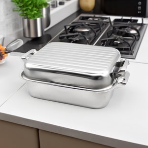 以下が含まれることがあります： 蓋付きのステンレス製のローストパン。パンはリブ付きのデザインで、両側に2つのハンドルが付いています。蓋の上には2つのハンドルが付いています。