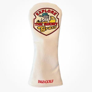May include: White golf club head cover with a red, yellow and blue embroidered patch that says "Explore the Short Grass" with a cartoon character in a canoe. The bottom of the cover has the text "B&B Golf" in red.
