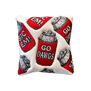 Könnte beinhalten: Weißer Golfschlägerkopfbezug mit einem Muster aus roten Limonaden-Dosen. Die Dosen haben silberne Deckel und den Text "GO DAWGS" und "SIC EM!". Der Hintergrund ist weiß.