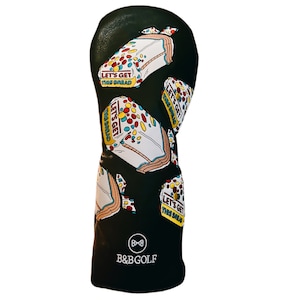 Puede incluir: Cubierta negra para la cabeza del palo de golf con un patrón de paquetes de pan coloridos. Los paquetes tienen el texto "Let's Get This Bread". La cubierta tiene un logotipo de pajarita blanca y el texto "B&BGOLF" en la parte inferior.