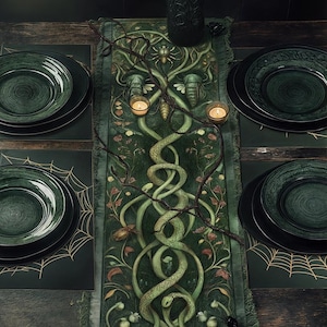 May include: A dark green table runner with a woven design featuring snakes, spiders, and vines. The runner is decorated with gold accents and has a fringed edge. Two small candles are placed on the runner.