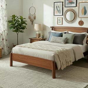 May include: A bedroom scene featuring a wooden bed frame with a neutral-toned comforter and pillows. The room includes a patterned rug, a potted plant, and artwork on the wall. Two wooden nightstands with lamps flank the bed.