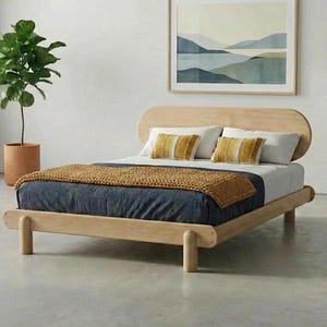 May include: A wooden bed frame with a curved headboard and four legs. The bed is made up with a navy blue duvet, a mustard-coloured throw blanket, and two yellow and white striped pillows. A framed landscape painting hangs above the bed.