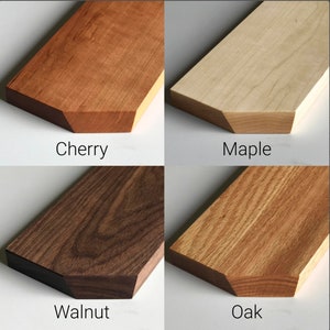 May include: Close-up of four wood samples: cherry, maple, walnut, and oak. Each sample is a light brown to dark brown color with a natural wood grain pattern.