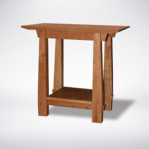 May include: A wooden end table with a shelf. The table is made of cherry wood and has a natural finish. The table is 24 inches wide, 16 inches deep, and 28 inches tall.