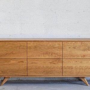 May include: A wooden cabinet with six drawers and tapered legs. The cabinet is made of light brown wood with a natural finish.