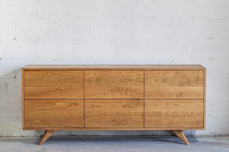 May include: A wooden cabinet with six drawers and tapered legs. The cabinet is made of light brown wood with a natural finish.
