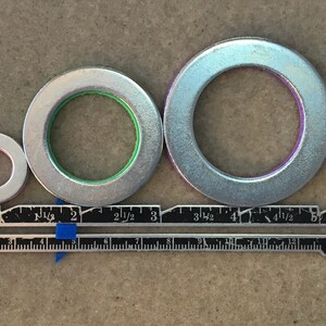 Puede incluir: Tres arandelas met&aacute;licas plateadas de diferentes tama&ntilde;os, con anillos interiores de color rojo, verde y morado. Una regla con medidas en pulgadas y cent&iacute;metros se coloca debajo. La regla est&aacute; marcada con el texto "Dritz Sewing Gauge".