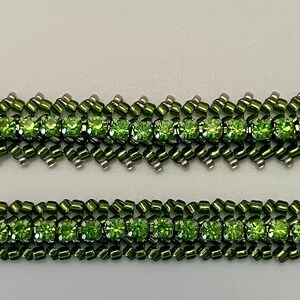 May include: Two beaded bracelets with a repeating pattern of olive green beads and square, light green gemstones. The bracelets have a zig-zag design and are set against a light gray background.