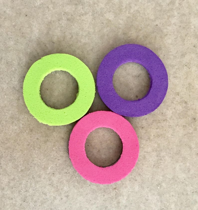Puede incluir: Tres anillos de espuma de colores, verde lima, morado y rosa. Cada anillo tiene un agujero circular en el centro. Los anillos est&aacute;n dispuestos en un patr&oacute;n triangular sobre un fondo neutro.