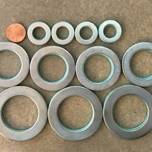 Puede incluir: Surtido de arandelas met&aacute;licas plateadas de varios tama&ntilde;os, con una moneda para comparar el tama&ntilde;o. Las arandelas tienen un anillo interior azul claro. Dispuestas en filas sobre una superficie neutra. Medidas en cm.