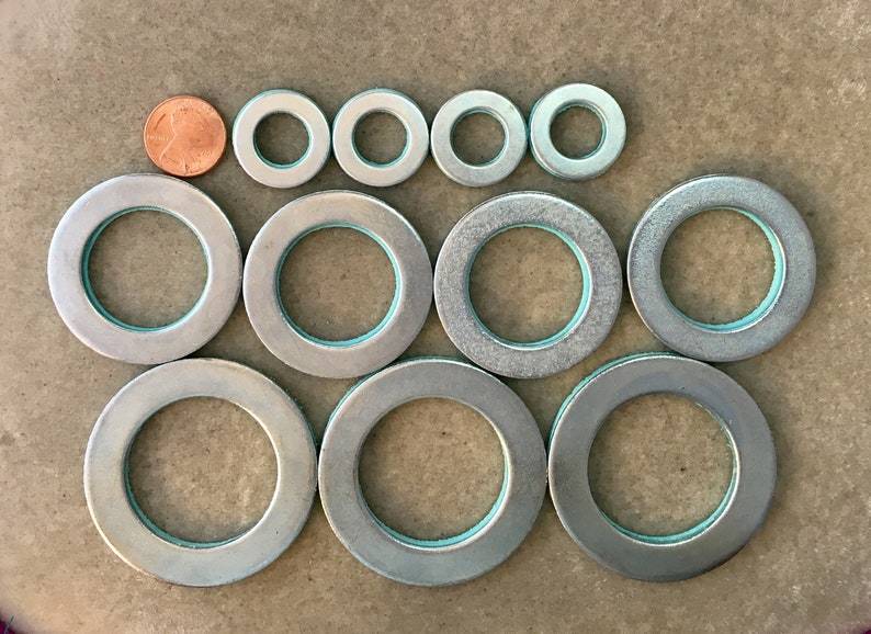 Puede incluir: Surtido de arandelas met&aacute;licas plateadas de varios tama&ntilde;os, con una moneda para comparar el tama&ntilde;o. Las arandelas tienen un anillo interior azul claro. Dispuestas en filas sobre una superficie neutra. Medidas en cm.