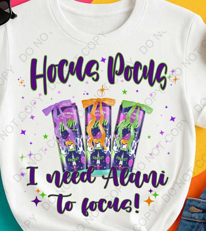 Op de afbeelding: Wit T-shirt met de tekst "Hocus Pocus" in paars en groen. Onder de tekst staan drie energiedrankblikjes met strikken. De tekst "I need Alani to focus!" staat eronder.