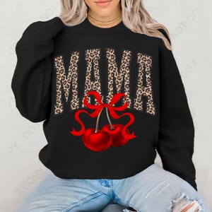 Puede incluir: Sudadera negra con la palabra "MAMA" en estampado de leopardo con un lazo rojo y dos cerezas rojas.