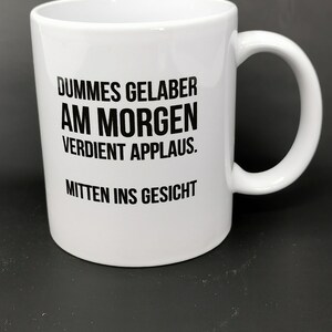 Könnte beinhalten: Weiße Keramiktasse mit schwarzem Text, der "DUMMES GELABER AM MORGEN VERDIENT APPLAUS. MITTEN INS GESICHT" lautet.