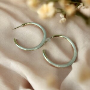 May include: A pair of silver hoop earrings with a light blue enamel finish.