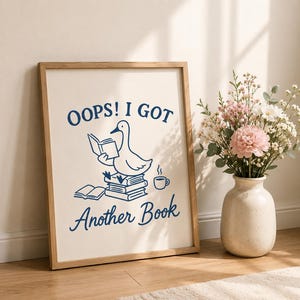 May include: A framed wall art print featuring a dark blue line drawing of a goose sitting on a stack of books while reading, with the text OOPS! I GOT ANOTHER BOOK printed in dark blue, accompanied by a small cup of coffee and an open book.