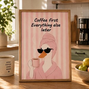 May include: A framed wall art print featuring a cartoon duck wearing a pink bathrobe and a matching towel wrap on its head, holding a pink coffee mug and wearing black sunglasses. The text Coffee first Everything else later is printed above.