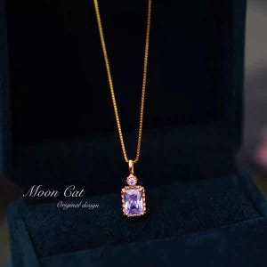 May include: A gold-colored necklace with a rectangular, light purple gemstone pendant. The pendant is set in a gold frame and hangs from a delicate gold chain. The text "Moon Cat Original design" is visible.