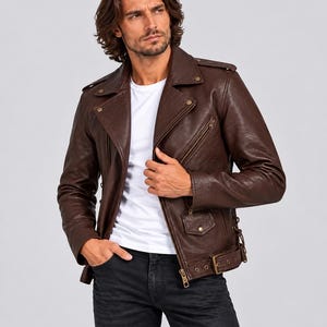 May include: A dark brown leather motorcycle jacket featuring a wide notched collar, metallic snap buttons, a diagonal front zip, and a buckled waist belt. The jacket includes side lacing details and zipped pockets, worn over a plain white t-shirt.