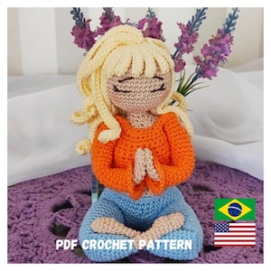Pode incluir: Padrão de crochê para uma boneca de mulher meditando com cabelo loiro, vestindo uma camisa laranja e calças azuis. A boneca está sentada em posição de lótus com as mãos em oração. O padrão está disponível em inglês e português.