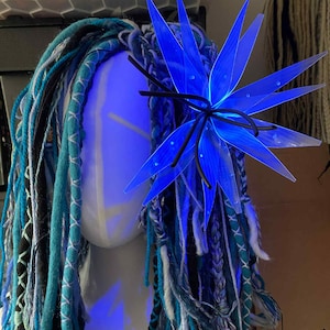Könnte beinhalten: Ein Schaufensterpuppenkopf mit blauen und türkisfarbenen Dreadlocks, verziert mit einem großen, leuchtenden blauen sternförmigen Accessoire. Die Dreadlocks sind mit weißen und schwarzen Akzenten verziert.