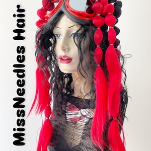 May include: A mannequin head with black hair, red accents, and goggles. The hair is styled with red and black elements, including long red strands and red ball-shaped decorations. The goggles are red and gray.