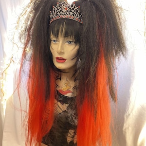 May include: A mannequin head with a black wig featuring orange streaks and a black crown with red accents. The wig has two high pigtails. The mannequin has red lipstick and a tattoo on its chest.