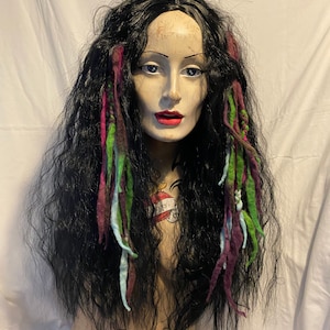Op de afbeelding: Een zwart pruik met lang, golvend haar en kleurrijke wollen dreadlocks. De dreadlocks zijn in tinten paars, groen, blauw en wit.