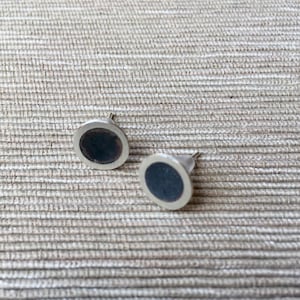 May include: A pair of silver-toned round earrings with black centers. The earrings have a simple, modern design.
