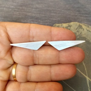 May include: A pair of silver triangle stud earrings. The earrings are brushed and have a matte finish.
