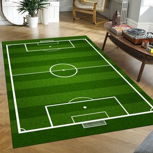 May include: A green and white area rug with a soccer field design. The rug features a green field with white lines marking the boundaries of the field, a center circle, and two goal boxes.