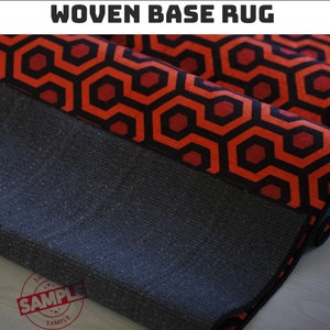 May include: A woven rug with a geometric pattern in red and black on top of a gray woven base. The rug is rolled up and the pattern is visible on the top of the roll.