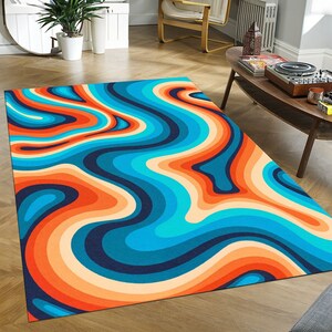 May include: A rectangular area rug with a retro, psychedelic design. The rug features flowing, wavy stripes in shades of orange, peach, blue, and navy. The pattern creates a sense of movement and visual interest, suitable for a living room or bedroom.