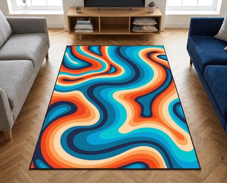 May include: A rectangular area rug with a vibrant, retro-inspired design. The rug features a swirling pattern of blue, orange, and cream-colored waves, bordered by a black edge. The rug is placed on a hardwood floor, adding a pop of color to the room.