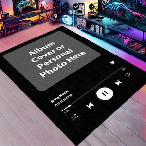 Puede incluir: Alfombra rectangular negra con un diseño de interfaz de reproductor de música. La alfombra presenta un cuadrado gris con el texto "Album Cover or Personal Photo Here". Debajo, muestra "Song Name" y "Artist Name". El diseño incluye controles de reproducción, pausa, salto y volumen.