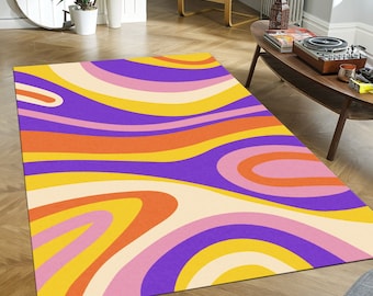 May include: A rectangular area rug with a retro design. The rug features a wavy pattern of yellow, orange, purple, pink, and cream stripes. The rug is placed on a wooden floor.