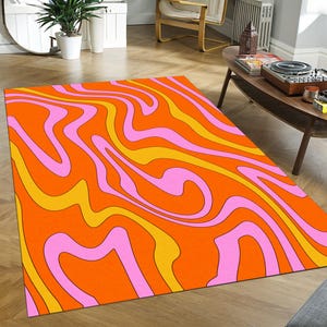 May include: A rectangular rug with a vibrant, retro design. The rug features a swirling pattern of orange, yellow, and pink, creating a psychedelic effect. The rug is placed on a wooden floor, adding warmth to the room. This rug is a statement piece for any living space.