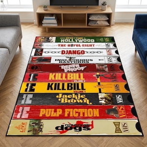 May include: A rectangular area rug featuring a design of stacked VHS tapes. The tapes display movie titles like "Pulp Fiction," "Kill Bill," and "Django." The rug has a black border and is placed on a wooden floor.