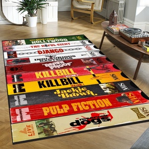 Puede incluir: Una alfombra colorida con un diseño de cintas VHS vintage con los títulos de películas populares, incluyendo "Pulp Fiction", "Reservoir Dogs", "Kill Bill", "Jackie Brown", "Inglourious Basterds", "Death Proof", "Django Unchained", "The Hateful Eight" y "Once Upon a Time in Hollywood".