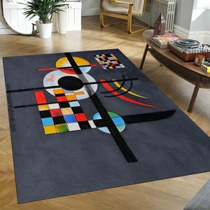 Puede incluir: Alfombra geométrica abstracta con formas negras, blancas, rojas, amarillas, azules y verdes sobre un fondo gris. La alfombra presenta círculos, cuadrados y líneas.