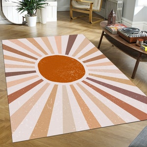 May include: A beige and brown area rug with a large orange sun design in the center. The sun has a textured look and is surrounded by radiating lines.