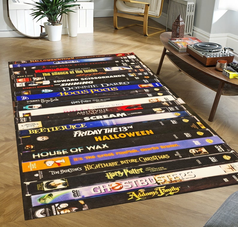 May include: A black and white rug featuring a design of classic Halloween movie VHS tapes. The tapes include titles such as "Halloween", "Beetlejuice", "Hocus Pocus", "Scream", "Friday the 13th", and "Nightmare Before Christmas".