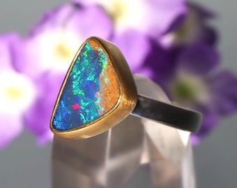 May include: A triangular opal ring set in gold with a silver band. The opal is a vibrant blue, green, and red.