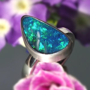 May include: A silver ring with a teardrop-shaped blue and green opal gemstone.