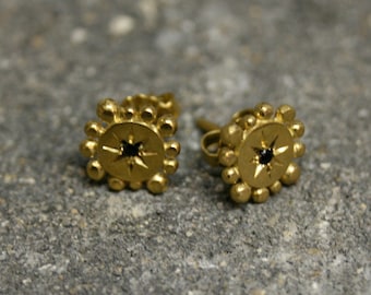 May include: A pair of gold earrings with a black star-shaped stone in the center of each earring. The earrings are surrounded by a circle of small gold beads.